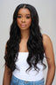 Woman with long, wavy black hair wearing a white top and blue jeans against a plain background